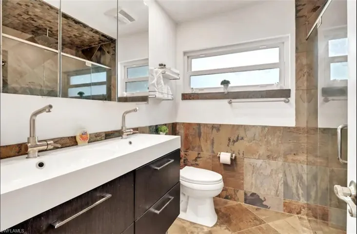 Bathroom with an enclosed shower, tile walls, toilet, and vanity
