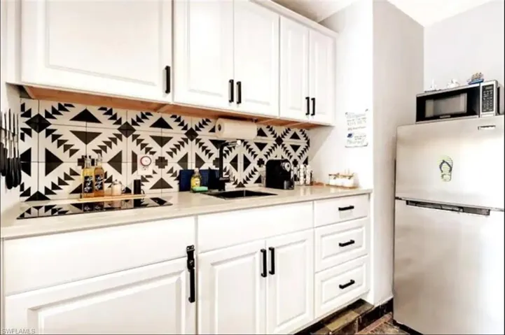 Kitchen with stainless steel appliances, sink, backsplash, and white cabinets