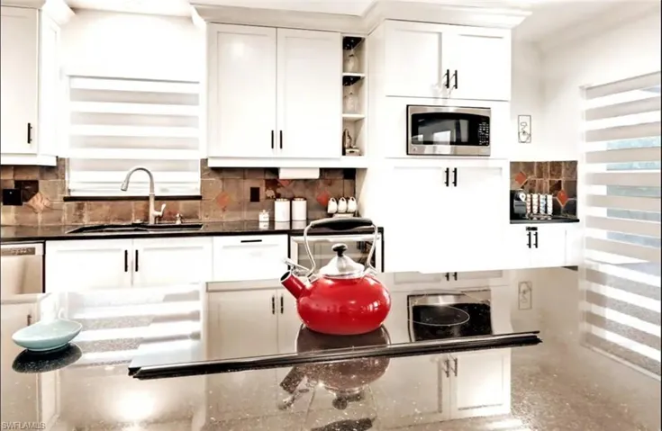 Kitchen featuring stainless steel appliances, sink, decorative backsplash, and white cabinets