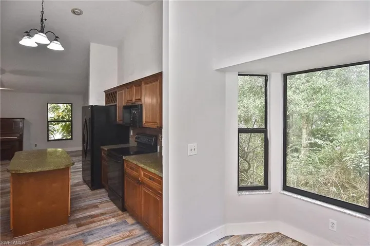 Kitchen featuring light stone counters, dark hardwood / wood-style flooring, hanging light fixtures, and black appliances