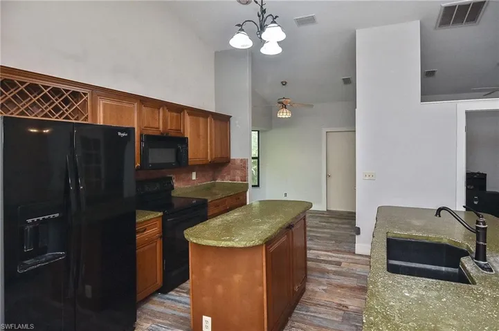 Kitchen with sink, wood-type flooring, a center island, pendant lighting, and black appliances