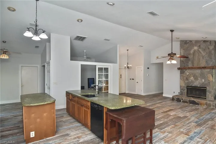Kitchen with a stone fireplace, hardwood / wood-style floors, dishwasher, an island with sink, and sink