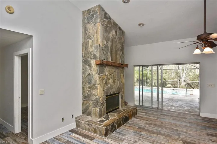 Living room with a stone fireplace, dark hardwood / wood-style floors, and ceiling fan