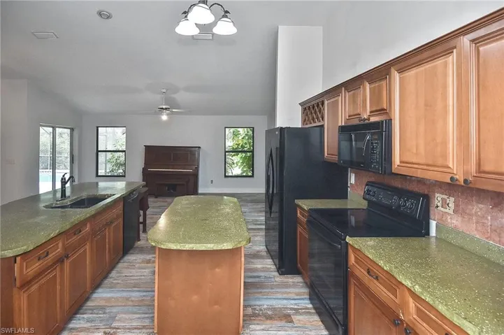 Kitchen with pendant lighting, sink, a kitchen island with sink, and black appliances
