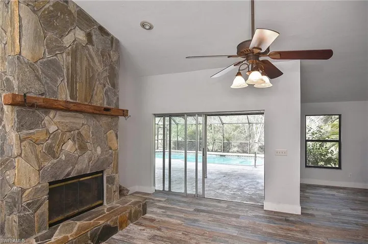 Living room with dark wood-type flooring, ceiling fan, lofted ceiling, and a stone fireplace