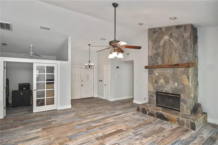 Living room featuring lofted ceiling, a stone fireplace, dark hardwood / wood-style floors, and ceiling fan