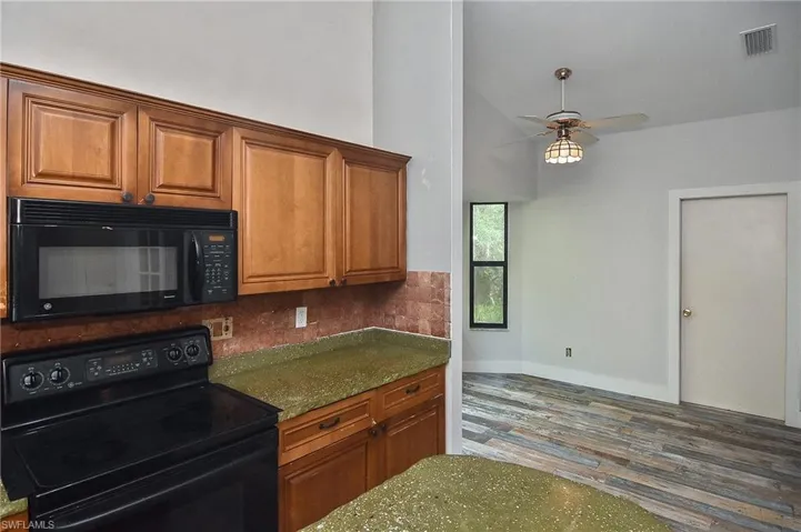 Kitchen with stone countertops, vaulted ceiling, hardwood / wood-style flooring, ceiling fan, and black appliances