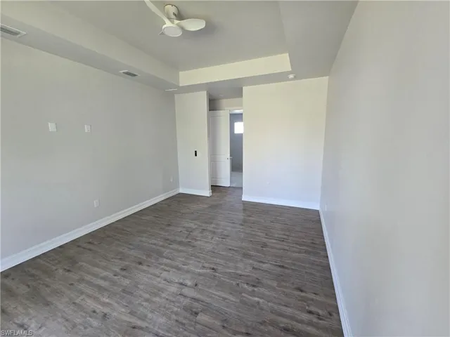 Unfurnished room featuring dark wood-style floors, a tray ceiling, and a ceiling fan