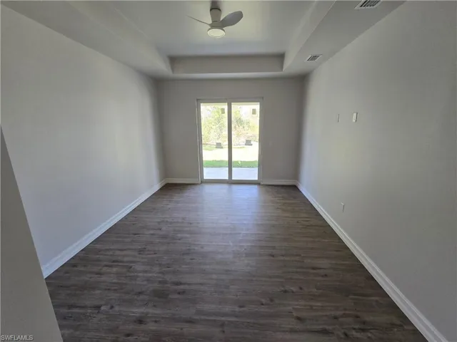 Master bedroom with a tray ceiling, dark wood-style floors, and a ceiling fan