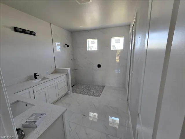 Full bath featuring a tile shower, vanity, and marble finish floors