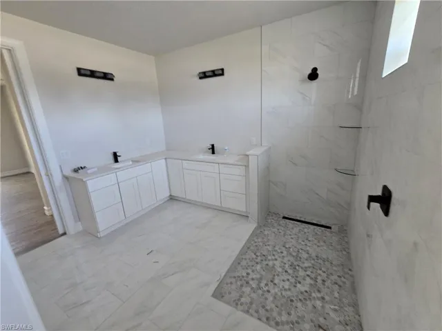 Bathroom with a walk in shower, double vanity, and marble look tile flooring