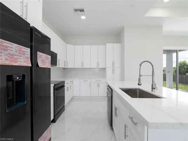 Kitchen featuring light tile patterned flooring, light stone counters, white cabinets, black appliances, and sink