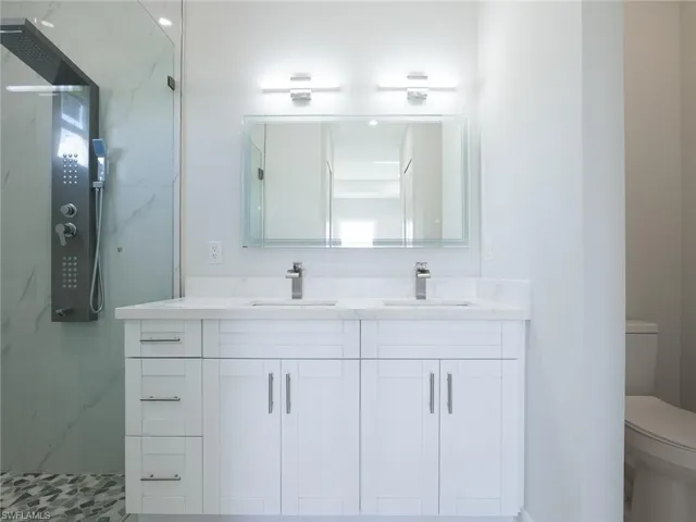 Bathroom featuring double vanity, toilet, a tile shower, and tile patterned flooring