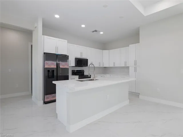 Kitchen featuring a center island with sink, light tile patterned flooring, white cabinets, black appliances, and sink