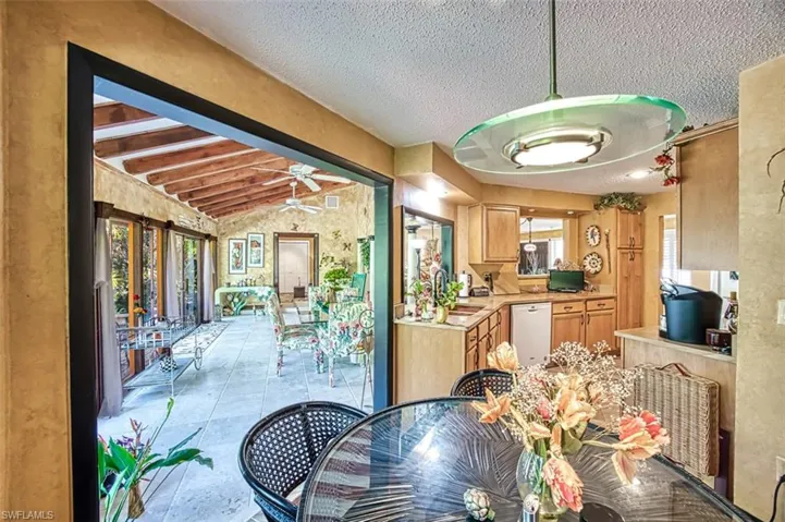 Dining area featuring sink, light tile patterned flooring, lofted ceiling with beams, a textured ceiling, and ceiling fan