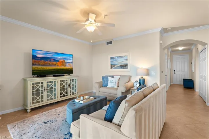 Tiled living room featuring visible vents, crown molding, baseboards, arched walkways, and a ceiling fan