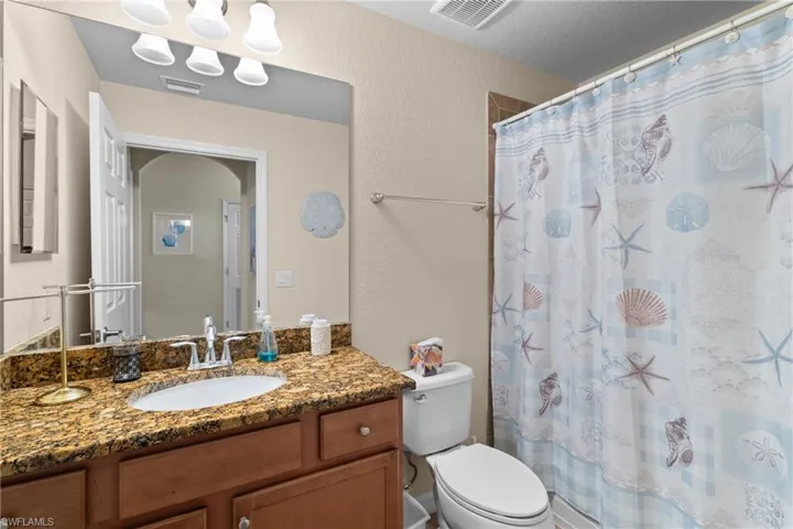 Full bath featuring visible vents, toilet, vanity, and a textured wall