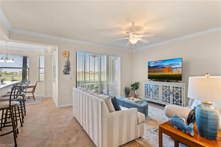 Living room with baseboards, light tile patterned flooring, crown molding, and ceiling fan with notable chandelier