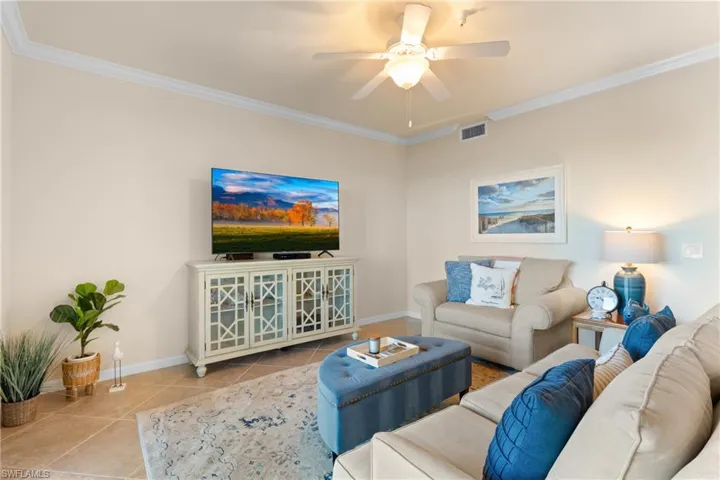 Living area featuring tile patterned flooring, ornamental molding, visible vents, and ceiling fan