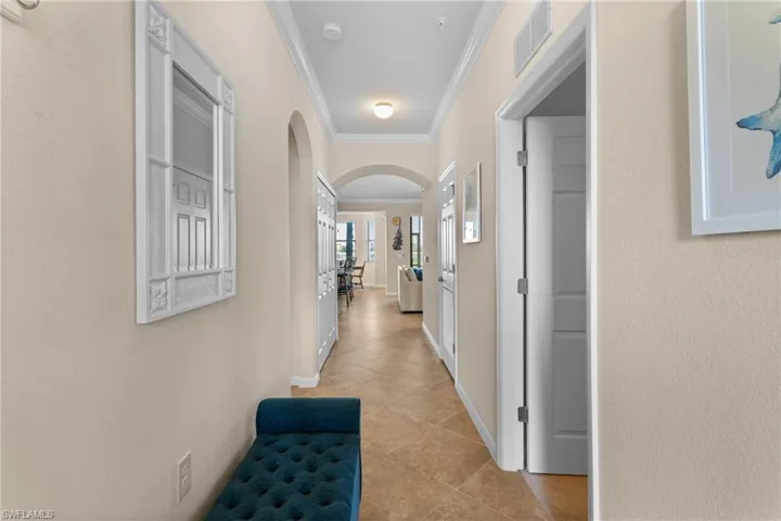 Corridor featuring visible vents, ornamental molding, arched walkways, light tile patterned flooring, and baseboards