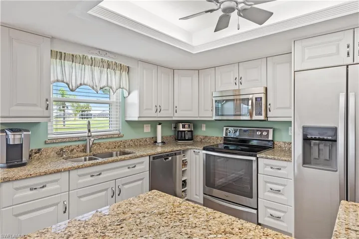 Kitchen featuring stainless steel appliances, white cabinets, sink, ceiling fan, and a raised ceiling