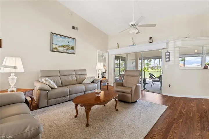 Living room with ceiling fan, dark wood-type flooring, and high vaulted ceiling