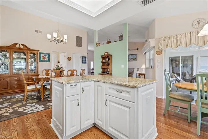 Kitchen with a chandelier, light wood-type flooring, white cabinets, light stone counters, and hanging light fixtures
