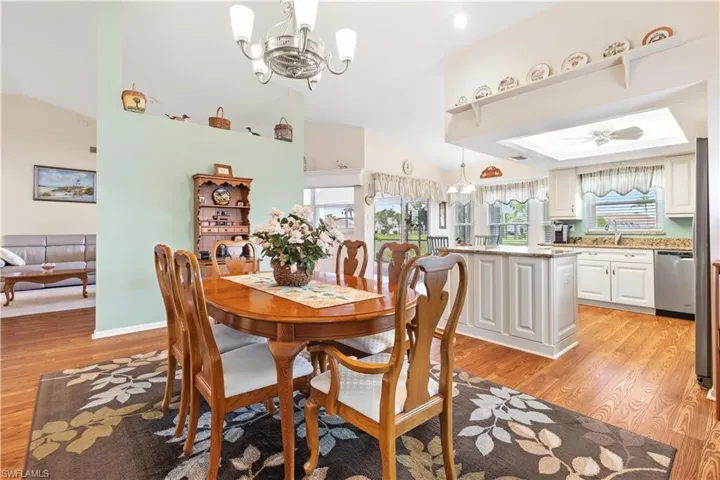 Dining area featuring vaulted ceiling, sink, light hardwood / wood-style floors, ceiling fan with notable chandelier, and a raised ceiling