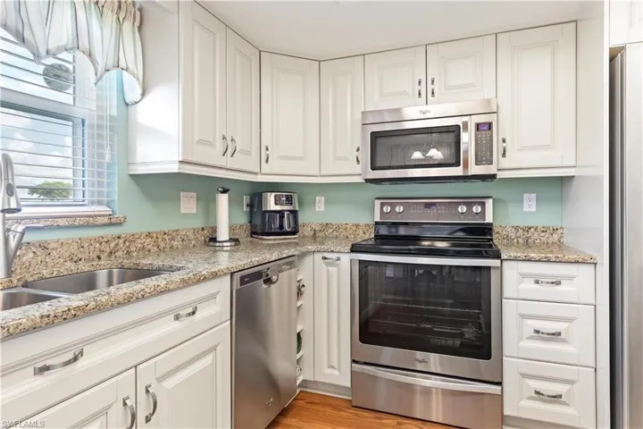 Kitchen with white cabinetry, light hardwood / wood-style flooring, appliances with stainless steel finishes, and light stone counters