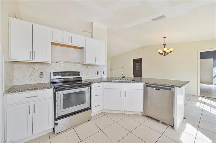 Kitchen featuring stainless steel appliances, white cabinets, dark stone countertops, backsplash, and vaulted ceiling