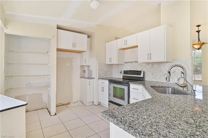 Kitchen with stainless steel range with electric cooktop, white cabinetry, tasteful backsplash, dark stone countertops, and light tile patterned floors