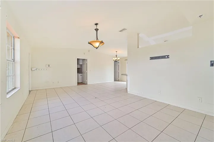 Empty room with hanging lights, light tile patterned floors, and vaulted ceiling