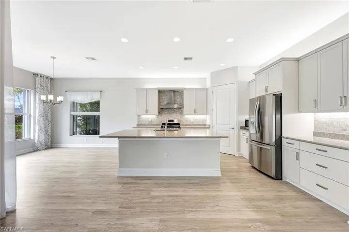 Kitchen featuring stainless steel appliances, an island with sink, wall chimney range hood, and light hardwood / wood-style flooring