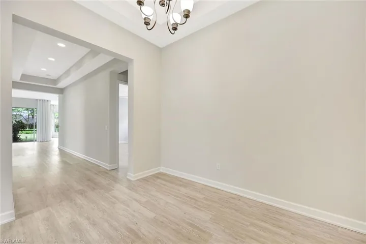 Spare room with an inviting chandelier, light hardwood / wood-style floors, and a raised ceiling