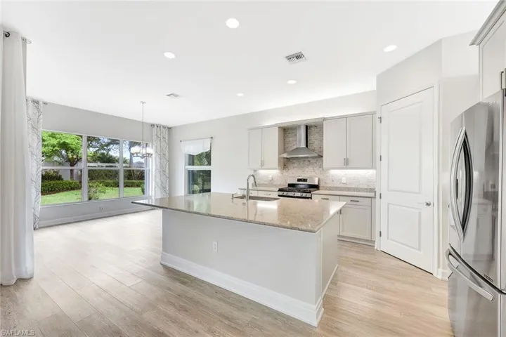Kitchen with sink, stainless steel appliances, a center island with sink, decorative light fixtures, and wall chimney exhaust hood