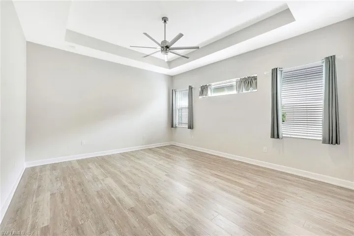Unfurnished room with a tray ceiling, ceiling fan, and light wood-type flooring