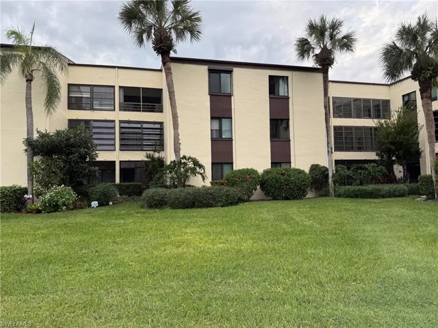 Cream-colored exterior with brown accents, multiple balconies, varied window styles, and tropical landscaping featuring palm trees