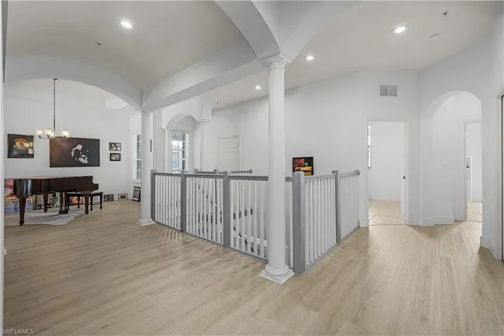 Corridor featuring lofted ceiling, arched walkways, laminate floors, recessed lighting, and decorative columns