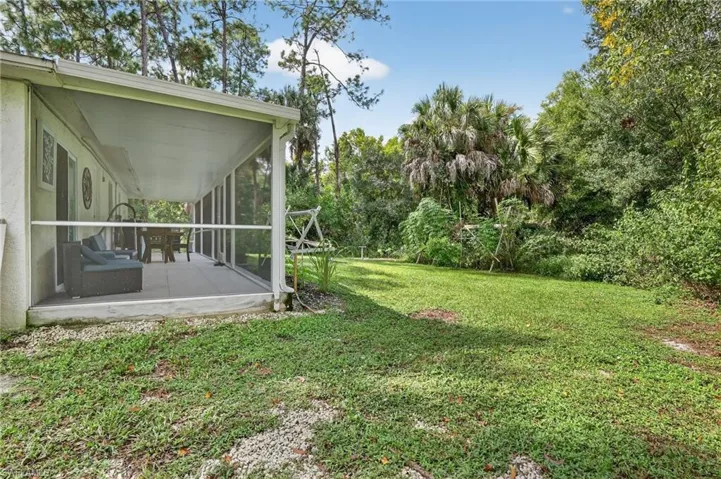 View of grassy yard featuring a sunroom and view of wooded area
