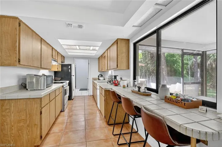 Kitchen with tile counters, light tile patterned floors, appliances with stainless steel finishes, a kitchen bar, and a skylight