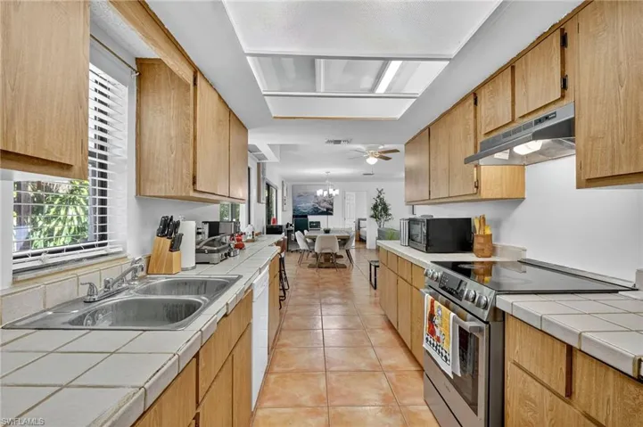 Kitchen featuring tile counters, stainless steel range with electric cooktop, light tile patterned floors, a chandelier, and under cabinet range hood