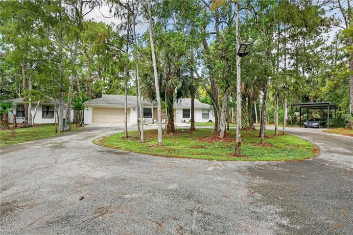 Ranch-style home with asphalt driveway, a front lawn, and view of scattered trees