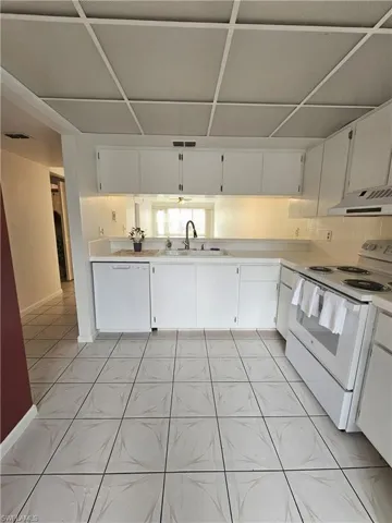 Kitchen featuring white appliances, white cabinetry, light countertops, and under cabinet range hood