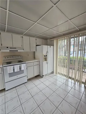 Kitchen with white appliances, white cabinetry, light countertops, range hood, and light tile patterned flooring