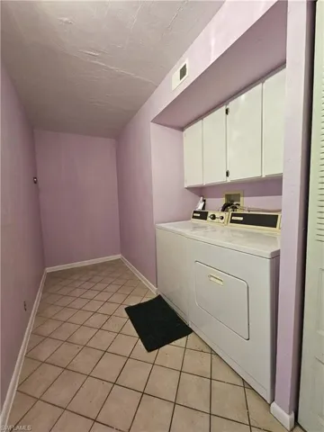 Washroom featuring washing machine and clothes dryer, cabinet space, light tile patterned flooring, and a textured ceiling