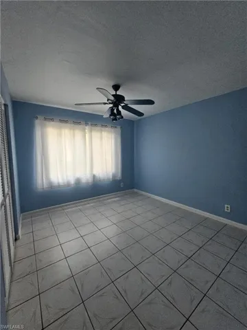 Empty room featuring a textured ceiling, a ceiling fan, and tile patterned floors