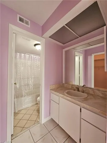Bathroom featuring vanity, light tile patterned floors, shower / tub combo with curtain, and a spacious closet