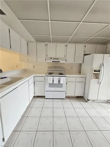 Kitchen with white appliances, light countertops, white cabinetry, light tile patterned floors, and ventilation hood
