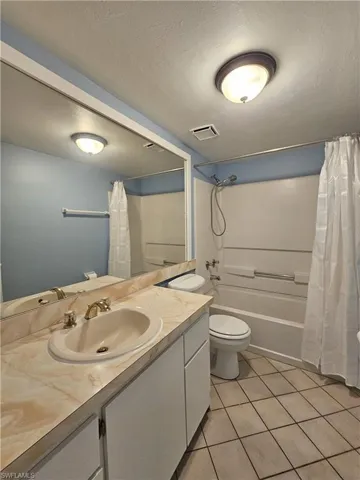 Bathroom featuring a textured ceiling, light tile patterned floors, shower / bathtub combination with curtain, and vanity