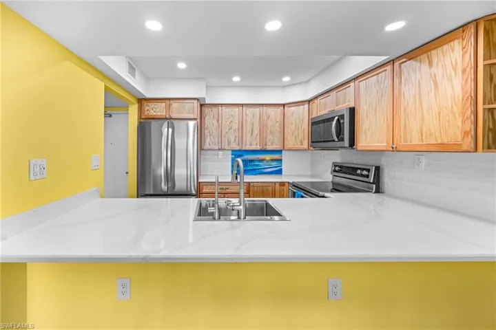 Kitchen with a peninsula, appliances with stainless steel finishes, tasteful backsplash, recessed lighting, and light stone counters